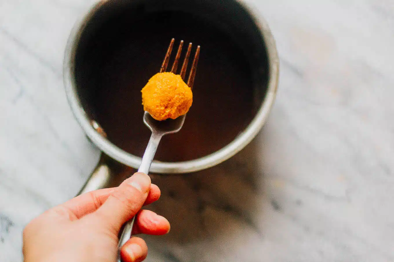 Sweet potato truffle centers being dipped in truffle sauce.